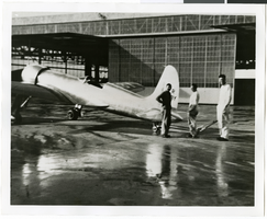 Photograph of men near a plane near an airplane hanger, 1930-1950