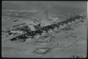 Black and white view of several industrial buildings, some are currently under construction. Temporary tent buildings are visible in the background.