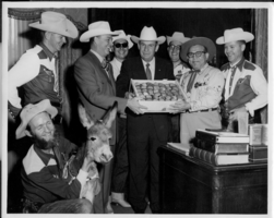 Group of men with a young burro.  Rex Bell is located left of center partially holding a box