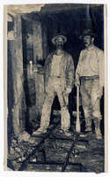 Photograph of two men standing on ore car rails inside a mine, Goldfield (Nev.), 1907