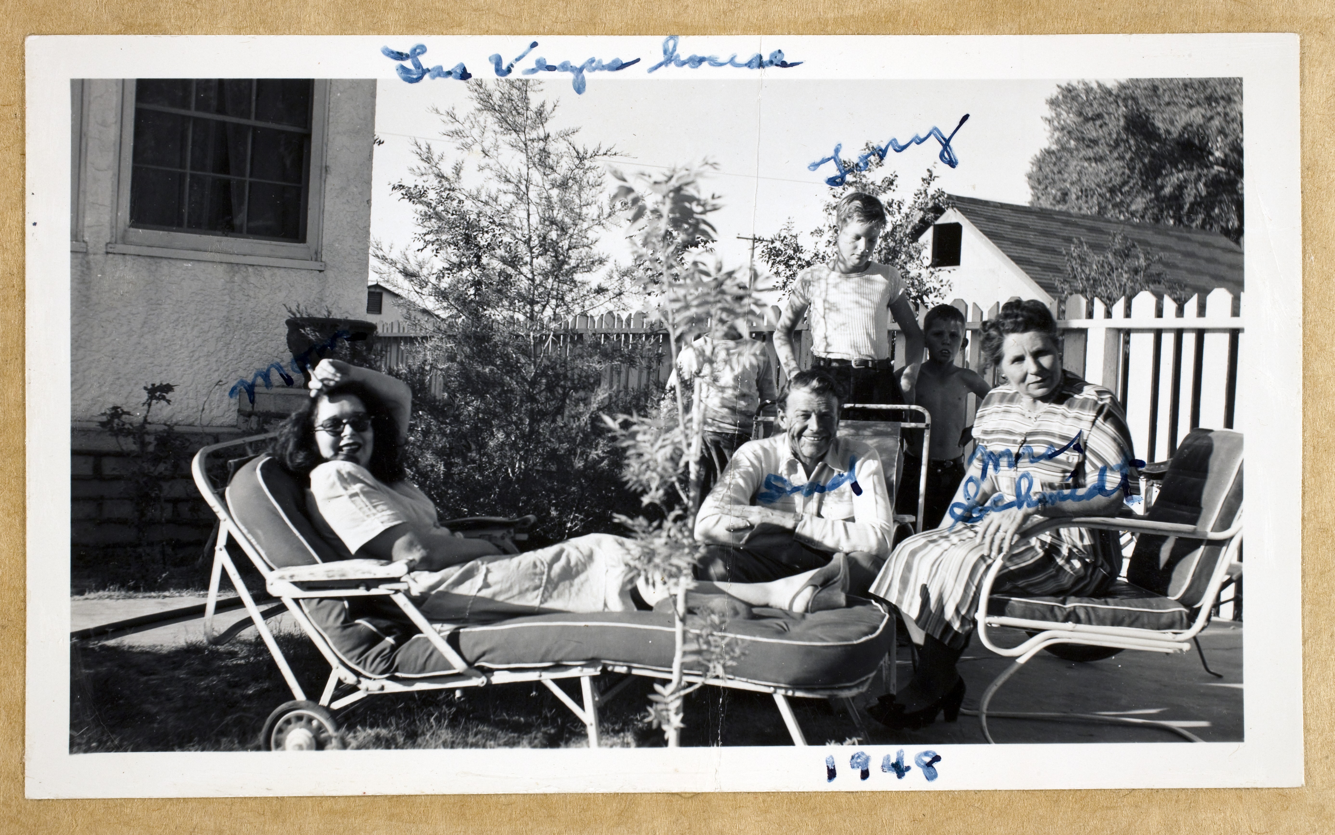 Left to right: Clara Bow , Rex Bell (George Francis Beldam), Rex Anthony Bell, Jr (Toni Larabow Beldam), George Francis Robert Bell, and Mrs Schmidt.  An unidentified child is behind a bush: photographic print