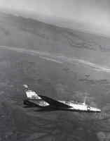 Black-and-white photograph of an F-100 airplane over Nellis Air Force Base, Nevada, circa mid 1950s