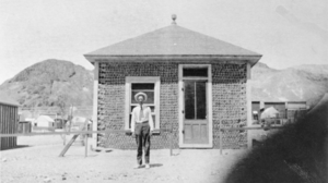 Film transparency of a man in front of the Bottle House in Beatty, Nevada, circa 1906