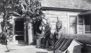 Photograph of men beside log houses, circa early 1920s-1940s