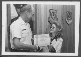 Black-and-white photograph of Colonel George A. Fox awarding Josephine Vos a certificate of appreciation, Nellis Air Force Base, Nevada, March 8, 1976