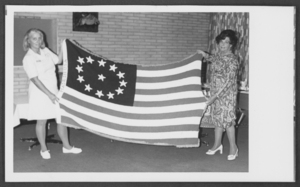 Photograph of two women holding up a Cowpens flag, Nellis Air Force Base, Nevada, July 29, 1976