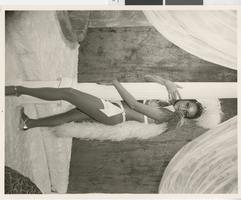 Photograph of a showgirl in a feathered costume, hugging a stage column, Dunes Hotel, Las Vegas (Nev.), 1957-1960s