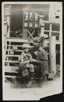 Hazel Denton's brother Ralph Baker sitting on a porch with a child on his lap: photographic print