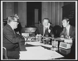 Howard Cannon on the phone with two unidentified men next to him: photographic print