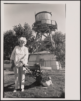 Marcelina Sandusky standing in backyard located within the original Sunrise Acres community with the water tower visible in the background: black-and-white photographs