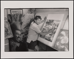 John Pacheco, portrait and commercial artist, stands inside his studio surrounded by his artwork: black-and-white photographs