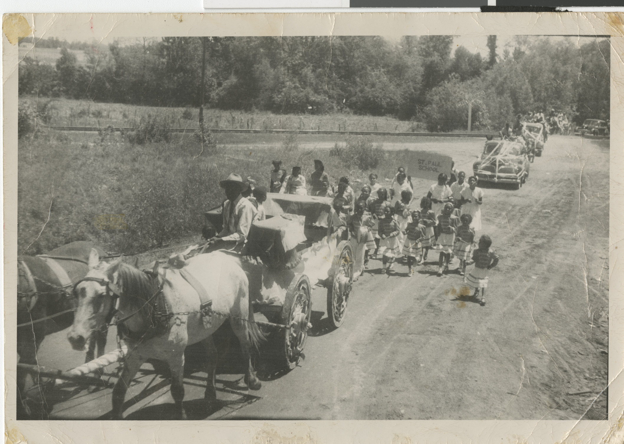Black and white photograph of a parade led by a horse-drawn carriage