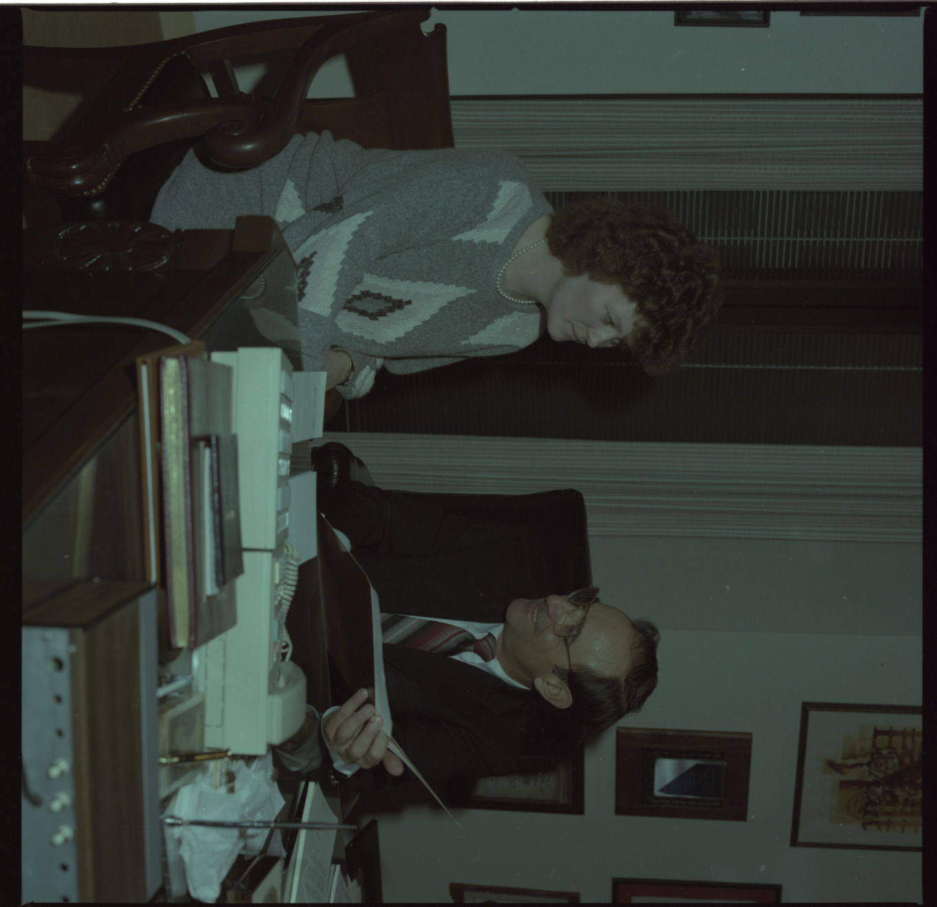 Film negative of Chic Hecht seated at a desk speaking with woman, February 26, 1988