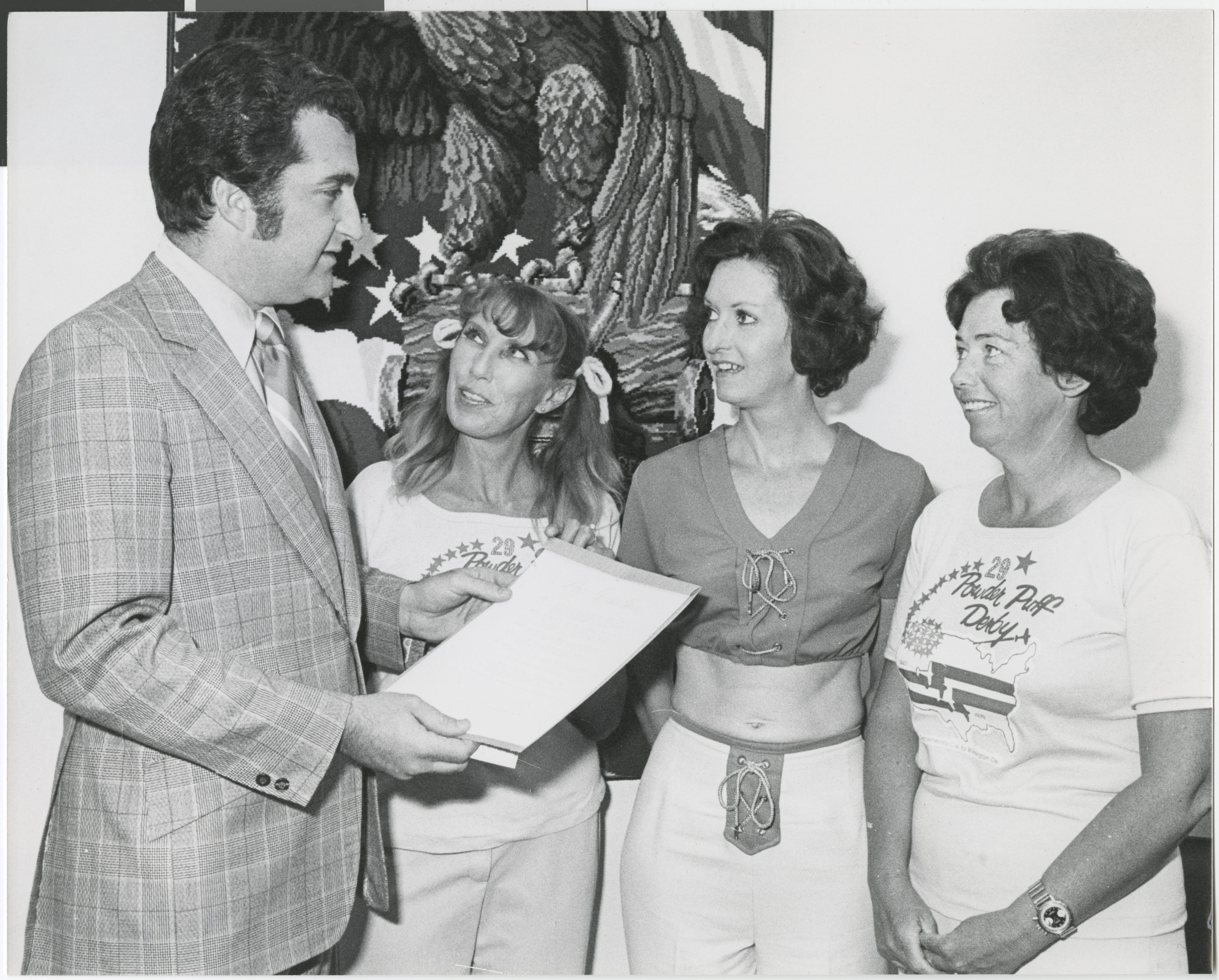 Photograph of Ron Lurie presenting a certificate to a group of women wearing Powder Puff Derby shirts